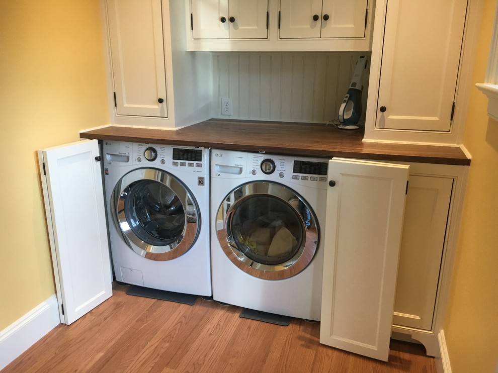 This is an example of a transitional laundry room in Dallas with white cabinets, wood benchtops, a side-by-side washer and dryer and brown benchtop.