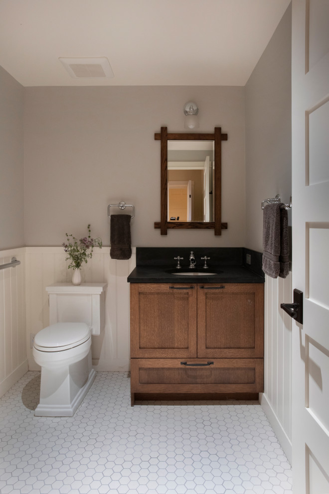 Cette photo montre un petit WC et toilettes craftsman avec un placard à porte shaker, des portes de placard marrons, WC séparés, un mur gris, un sol en carrelage de porcelaine, un lavabo encastré, un plan de toilette en quartz modifié, un sol blanc, un plan de toilette noir et meuble-lavabo encastré.