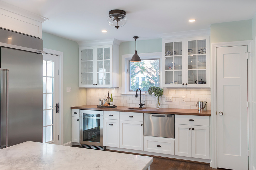 Photo of a large transitional l-shaped eat-in kitchen in DC Metro with a farmhouse sink, shaker cabinets, white cabinets, marble benchtops, white splashback, ceramic splashback, stainless steel appliances, medium hardwood floors and with island.
