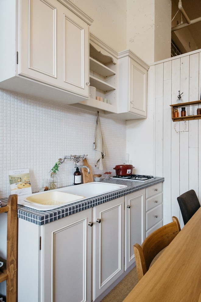 Photo of a small scandinavian single-wall eat-in kitchen in Other with a drop-in sink, beaded inset cabinets, white cabinets, stainless steel benchtops, white splashback, porcelain splashback and with island.