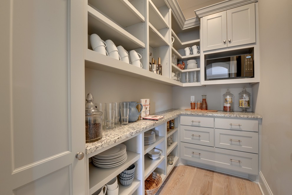 Large transitional l-shaped kitchen pantry in Minneapolis with a farmhouse sink, white cabinets, grey splashback, subway tile splashback, stainless steel appliances, light hardwood floors, with island and open cabinets.