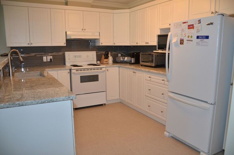Mid-sized transitional u-shaped vinyl floor open concept kitchen photo in Toronto with an undermount sink, raised-panel cabinets, white cabinets, quartzite countertops, gray backsplash, glass tile backsplash, white appliances and a peninsula