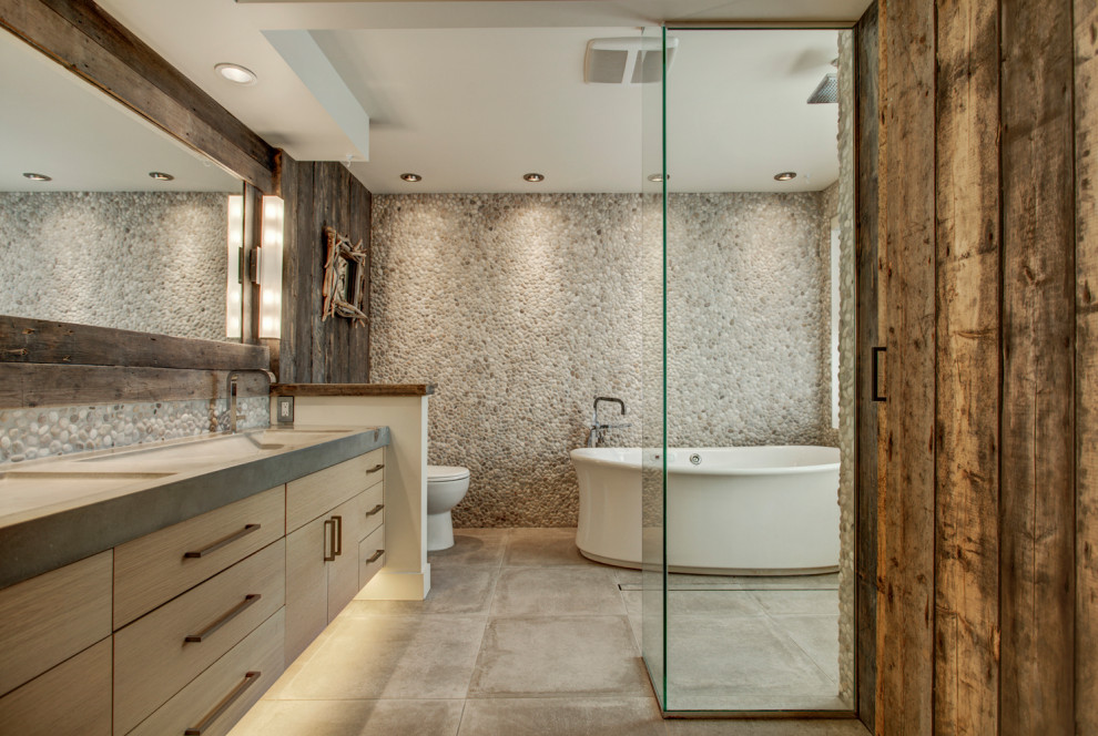 Large mountain style master gray tile cement tile floor, gray floor and double-sink walk-in shower photo with flat-panel cabinets, concrete countertops, gray countertops, light wood cabinets, brown walls, an undermount sink and a floating vanity