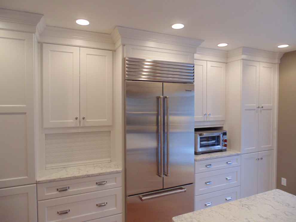 Example of a large transitional u-shaped medium tone wood floor and brown floor eat-in kitchen design with an undermount sink, recessed-panel cabinets, white cabinets, quartz countertops, white backsplash, subway tile backsplash, stainless steel appliances, an island and white countertops