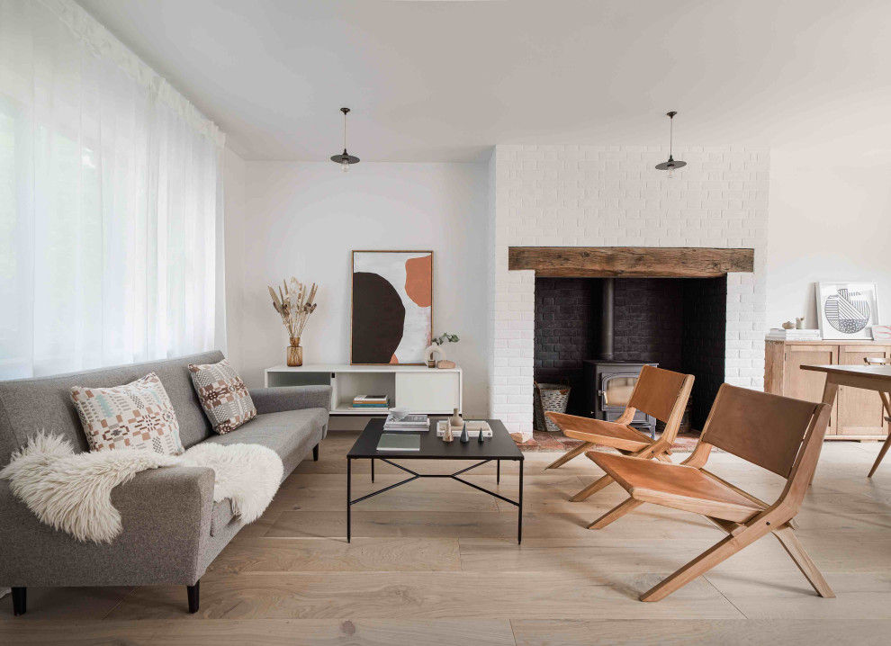 Photo of a mid-sized scandinavian formal open concept living room in Essex with white walls, light hardwood floors, a wood stove, a brick fireplace surround and no tv.