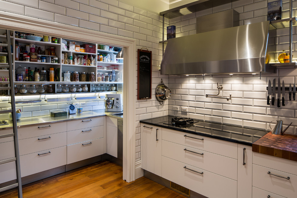 Inspiration for a large industrial l-shaped eat-in kitchen in Wellington with an undermount sink, glass-front cabinets, white cabinets, granite benchtops, white splashback, ceramic splashback, stainless steel appliances, medium hardwood floors and with island.