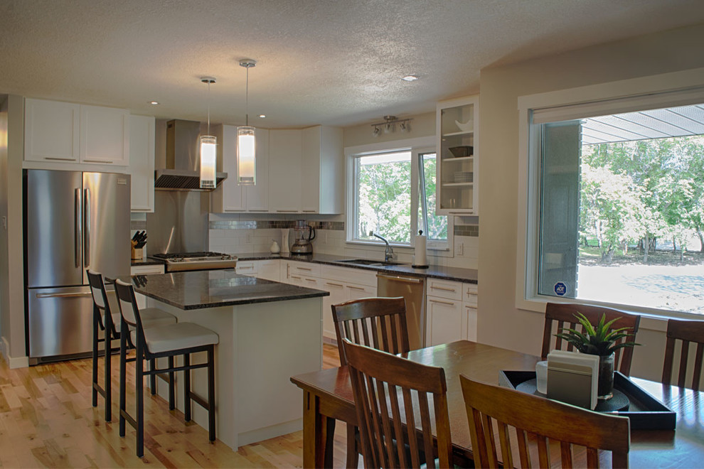 Eat-in kitchen - small transitional l-shaped light wood floor and beige floor eat-in kitchen idea in Calgary with a double-bowl sink, shaker cabinets, white cabinets, white backsplash, subway tile backsplash, stainless steel appliances and an island