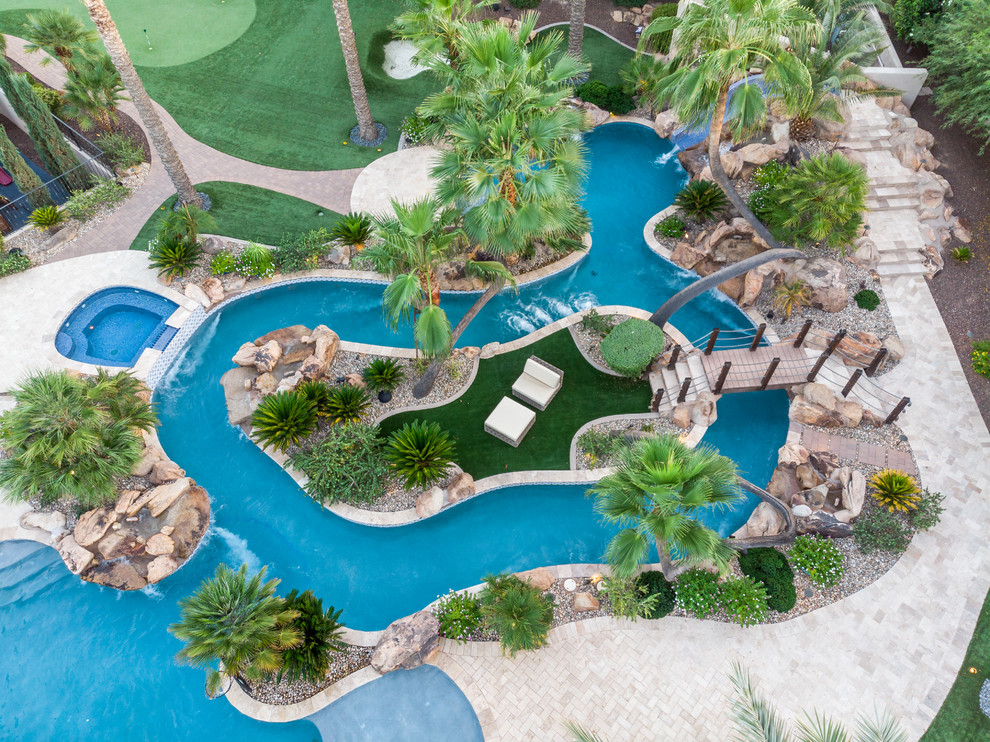 Large tropical backyard custom-shaped pool in Phoenix with a water slide and natural stone pavers.