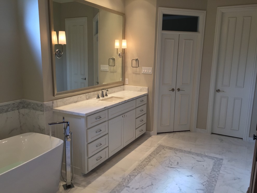 Photo of a large modern master bathroom in Dallas with an undermount sink, shaker cabinets, white cabinets, marble benchtops, a freestanding tub, a corner shower, a one-piece toilet, white tile, stone tile, white walls and marble floors.