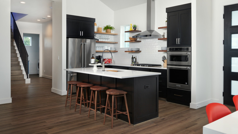 Photo of a contemporary l-shaped kitchen in Austin with an undermount sink, shaker cabinets, black cabinets, white splashback, subway tile splashback, stainless steel appliances, dark hardwood floors, with island, brown floor, white benchtop and vaulted.