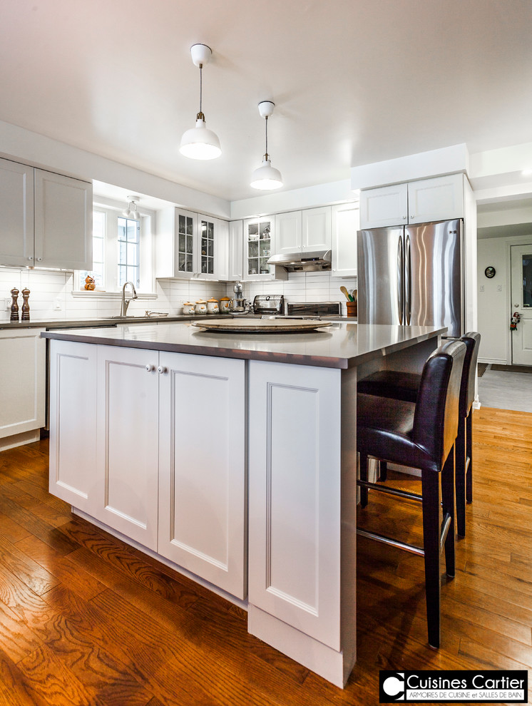 Inspiration for a large transitional medium tone wood floor eat-in kitchen remodel in Montreal with a double-bowl sink, shaker cabinets, white cabinets, quartzite countertops, white backsplash, ceramic backsplash, stainless steel appliances and an island