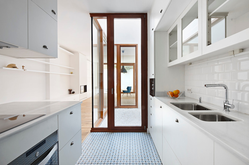 Mid-sized contemporary galley open plan kitchen in Barcelona with a double-bowl sink, flat-panel cabinets, white cabinets, marble benchtops, white splashback, ceramic splashback, stainless steel appliances, with island and blue floor.