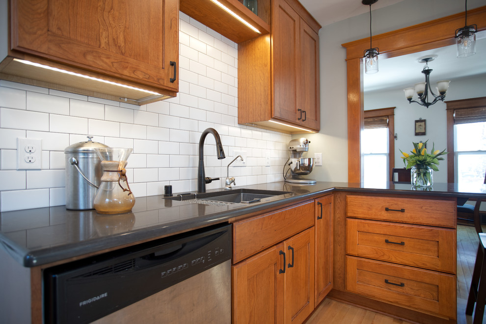 Mid-sized arts and crafts l-shaped eat-in kitchen in Minneapolis with an undermount sink, recessed-panel cabinets, medium wood cabinets, quartz benchtops, white splashback, ceramic splashback, stainless steel appliances, light hardwood floors, a peninsula, brown floor and grey benchtop.