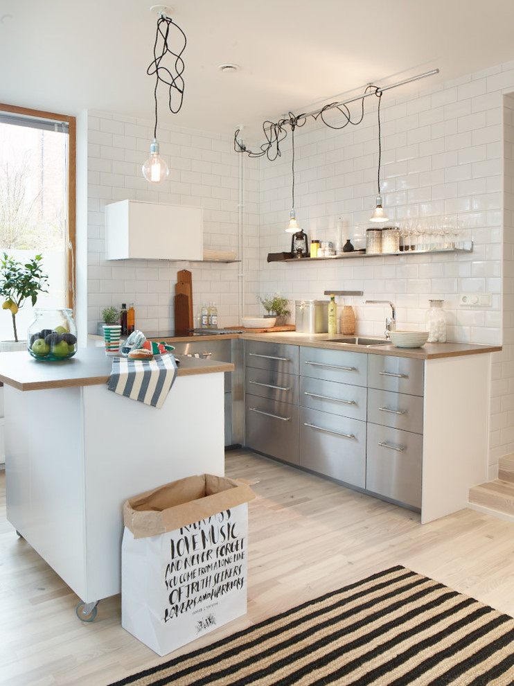 Design ideas for a mid-sized industrial galley kitchen in Stockholm with a single-bowl sink, flat-panel cabinets, stainless steel cabinets, wood benchtops, white splashback, ceramic splashback, light hardwood floors and no island.
