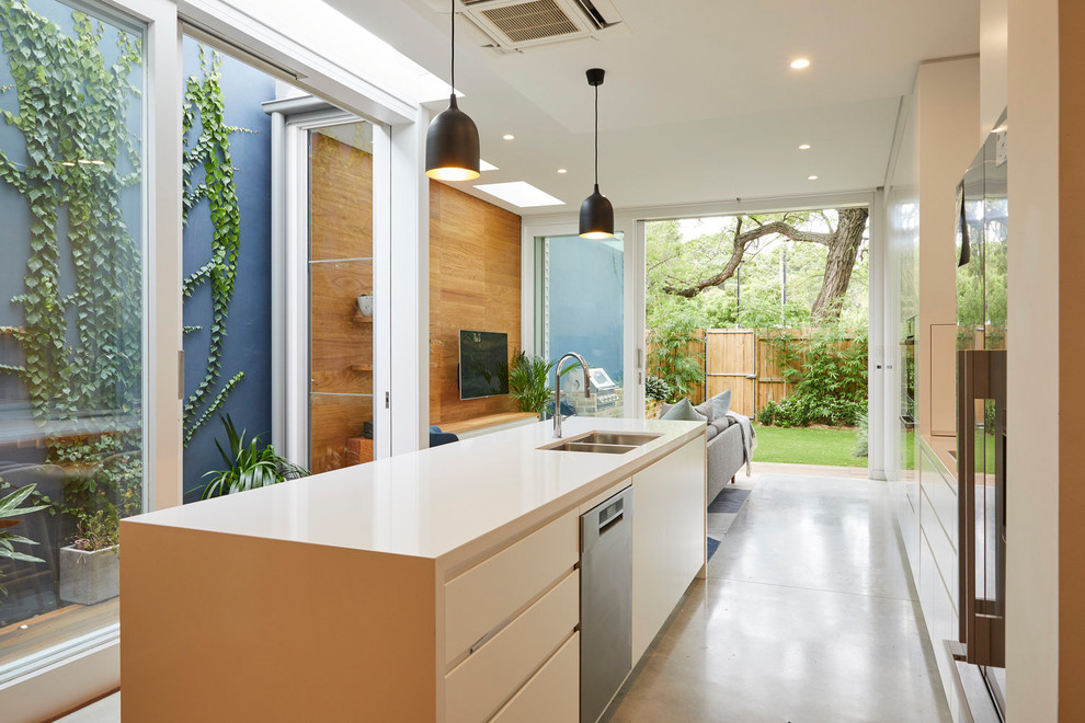 This is an example of a contemporary galley open plan kitchen in Wollongong with a double-bowl sink, flat-panel cabinets, white cabinets, concrete floors, with island, stainless steel appliances, grey floor and beige benchtop.
