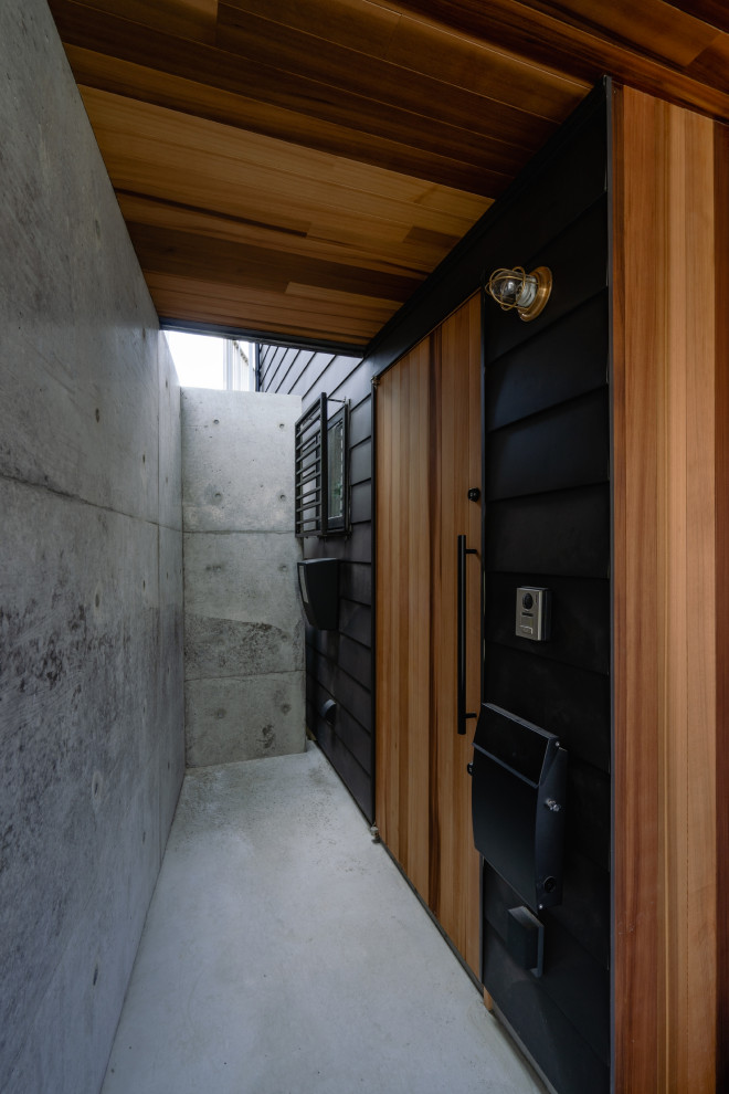 Réalisation d'une porte d'entrée minimaliste avec un mur noir, sol en béton ciré, une porte simple, une porte en bois brun, un sol gris et un plafond en bois.