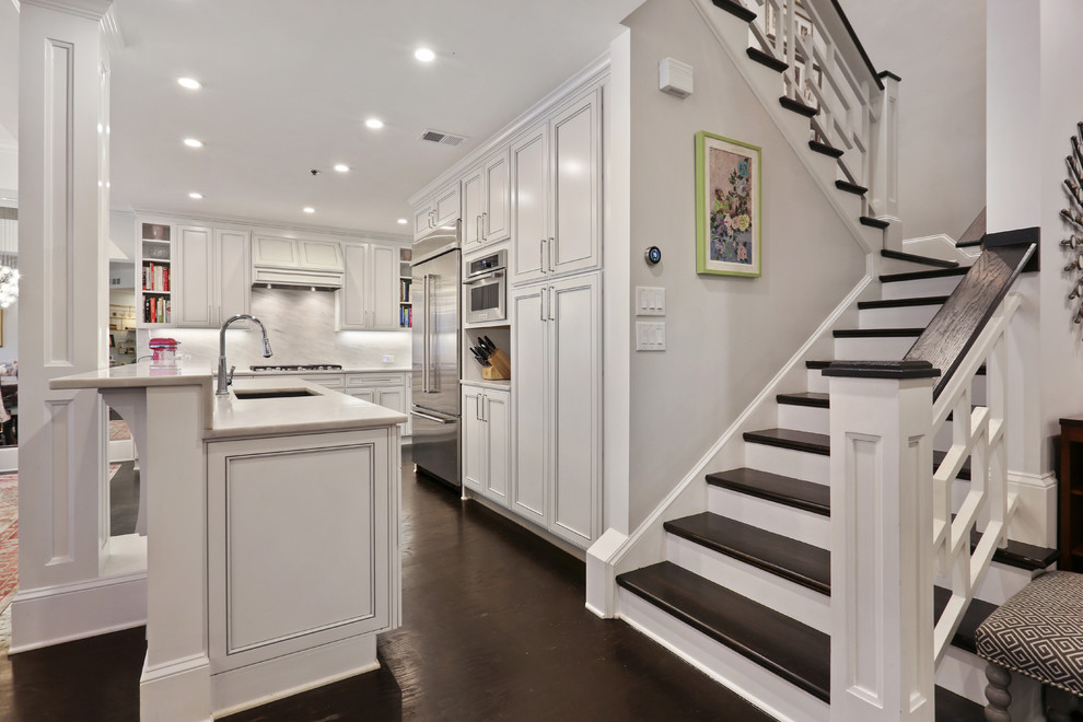 This is an example of a mid-sized eclectic l-shaped eat-in kitchen in Atlanta with white cabinets, marble benchtops, white splashback, marble splashback, stainless steel appliances, dark hardwood floors, with island, black floor, white benchtop and recessed-panel cabinets.