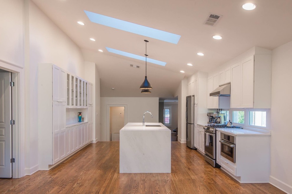 Open concept kitchen - mid-sized transitional single-wall light wood floor open concept kitchen idea in Atlanta with a double-bowl sink, recessed-panel cabinets, white cabinets, marble countertops, white backsplash, subway tile backsplash, stainless steel appliances and an island