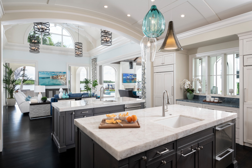 This is an example of a large beach style u-shaped eat-in kitchen in Other with an undermount sink, recessed-panel cabinets, dark wood cabinets, quartzite benchtops, stainless steel appliances, painted wood floors, multiple islands, brown floor and white benchtop.