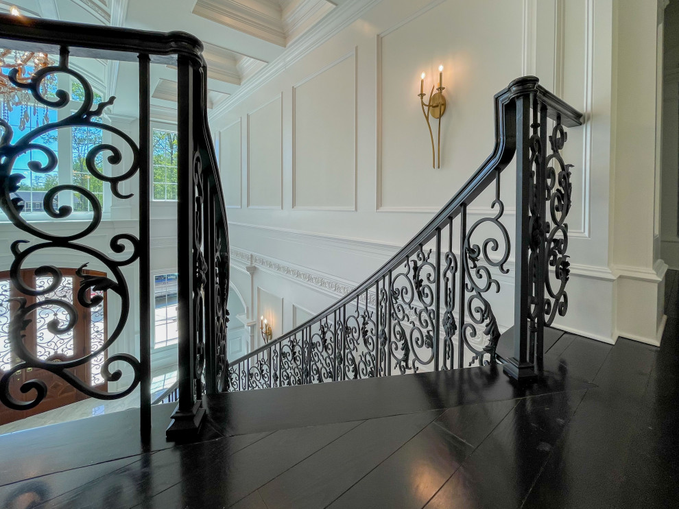 This is an example of an expansive classic wood curved mixed railing staircase in DC Metro with wood risers and wainscoting.