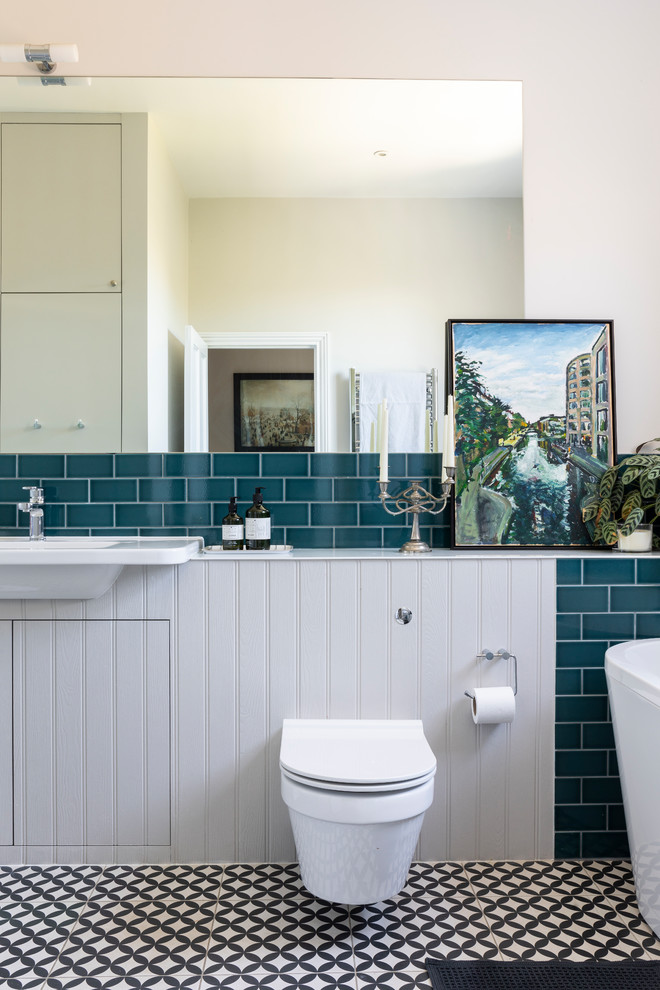 This is an example of a mid-sized contemporary 3/4 bathroom in London with a wall-mount toilet, grey walls, grey cabinets, multi-coloured floor, white benchtops, a freestanding tub, ceramic tile, cement tiles and a drop-in sink.
