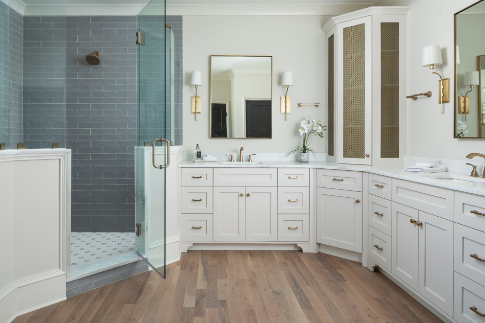 Inspiration for a mid-sized transitional master bathroom in Charlotte with grey cabinets, a freestanding tub, a corner shower, blue tile, glass tile, beige walls, medium hardwood floors, marble benchtops, brown floor, a hinged shower door, white benchtops, a double vanity and a built-in vanity.