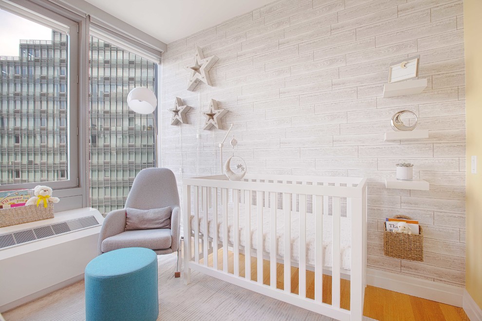 This is an example of a small contemporary gender-neutral nursery in New York with grey walls, light hardwood floors and brown floor.