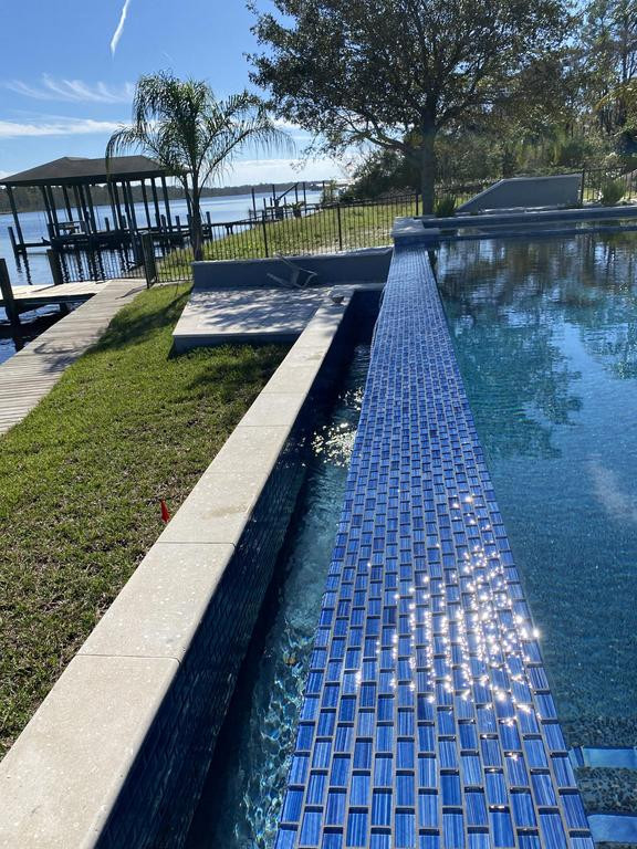 Foto di una piscina a sfioro infinito minimalista rettangolare di medie dimensioni e dietro casa con una vasca idromassaggio e pavimentazioni in pietra naturale