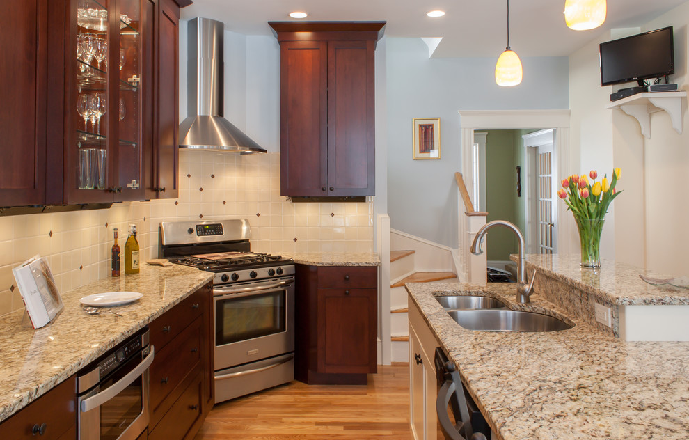Photo of a mid-sized traditional l-shaped eat-in kitchen in Boston with an undermount sink, recessed-panel cabinets, dark wood cabinets, granite benchtops, beige splashback, ceramic splashback, stainless steel appliances and medium hardwood floors.