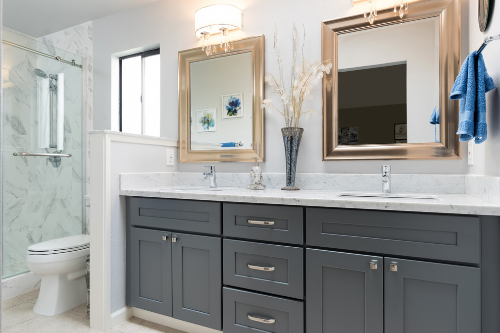 This is an example of a large transitional master bathroom in Other with shaker cabinets, grey cabinets, an alcove shower, a two-piece toilet, white tile, marble, beige walls, travertine floors, an undermount sink, quartzite benchtops, beige floor, a sliding shower screen and white benchtops.