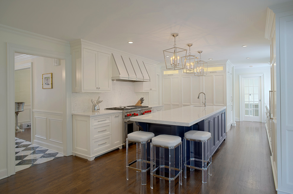 Photo of a medium sized classic u-shaped kitchen/diner in Chicago with a built-in sink, recessed-panel cabinets, white cabinets, engineered stone countertops, white splashback, engineered quartz splashback, stainless steel appliances, dark hardwood flooring, an island, brown floors and white worktops.