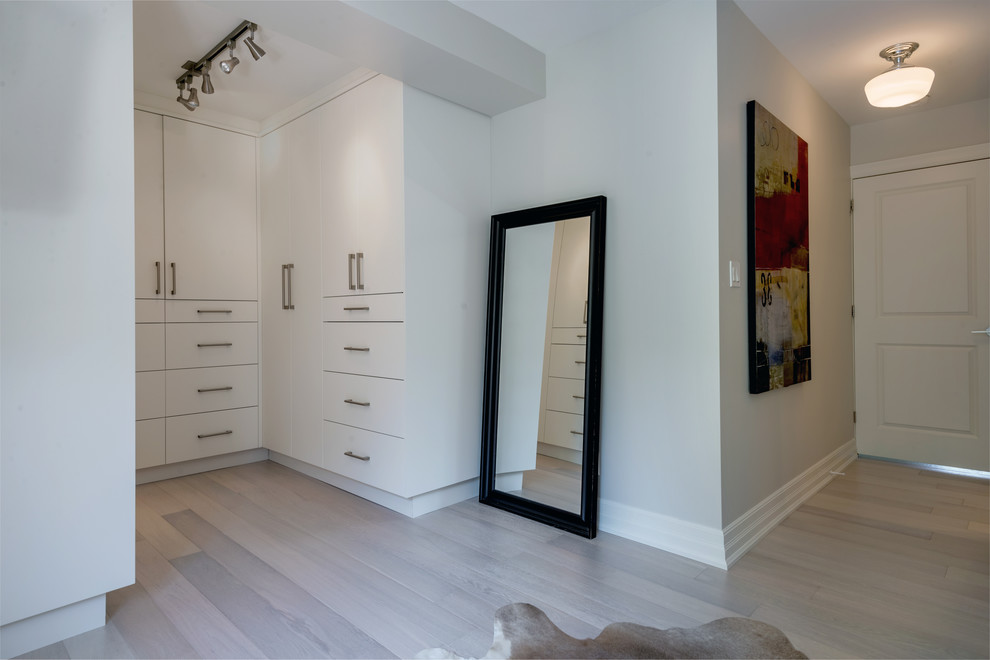 Photo of a small contemporary gender-neutral walk-in wardrobe in Toronto with flat-panel cabinets, white cabinets and light hardwood floors.
