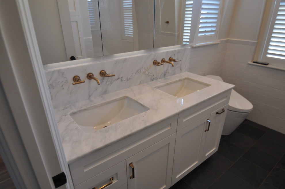 Design ideas for a medium sized traditional family bathroom in Boston with shaker cabinets, white cabinets, an alcove bath, an alcove shower, a wall mounted toilet, white tiles, porcelain tiles, white walls, slate flooring, a submerged sink, marble worktops, black floors, an open shower, white worktops, double sinks, a built in vanity unit and wainscoting.