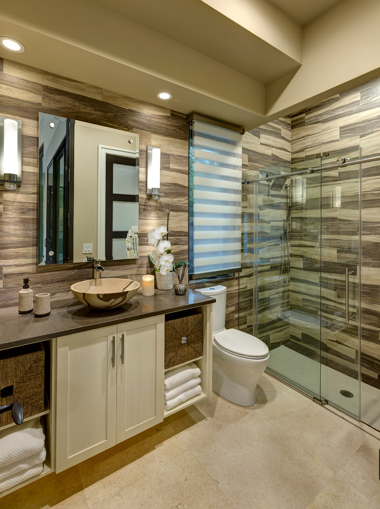Transitional bathroom in Orlando with a vessel sink, shaker cabinets, white cabinets, an alcove shower, a two-piece toilet, multi-coloured tile, beige walls and brown benchtops.