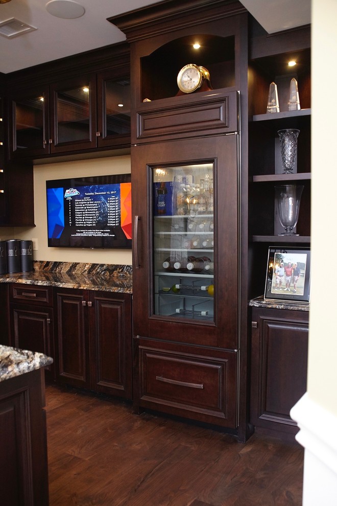 This is an example of a large traditional u-shaped wet bar in Boston with an undermount sink, raised-panel cabinets, dark wood cabinets, granite benchtops, beige splashback, dark hardwood floors and brown floor.