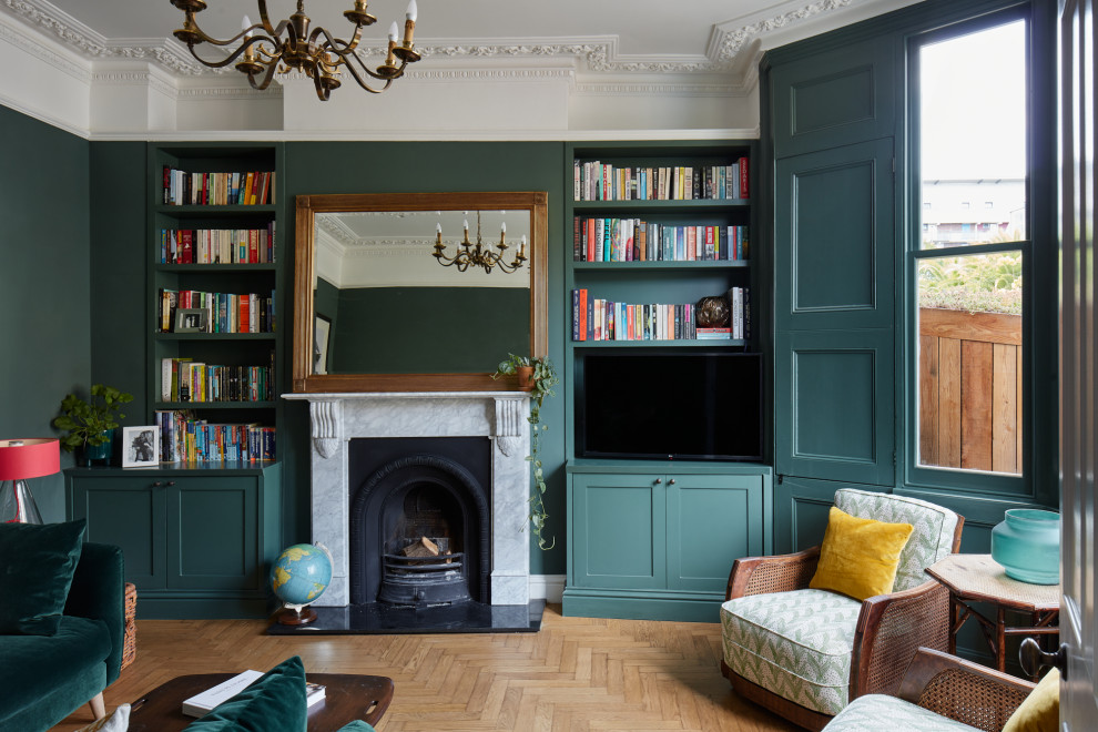 Idée de décoration pour un salon bohème de taille moyenne avec un mur vert, parquet clair, une cheminée standard, un manteau de cheminée en pierre, un téléviseur encastré et un sol beige.