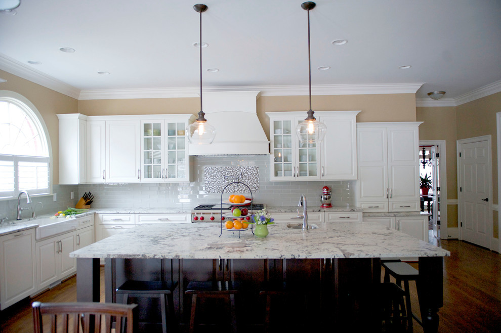 Open concept kitchen - mid-sized transitional l-shaped medium tone wood floor open concept kitchen idea in Atlanta with a farmhouse sink, raised-panel cabinets, white cabinets, granite countertops, gray backsplash, glass tile backsplash, stainless steel appliances and an island