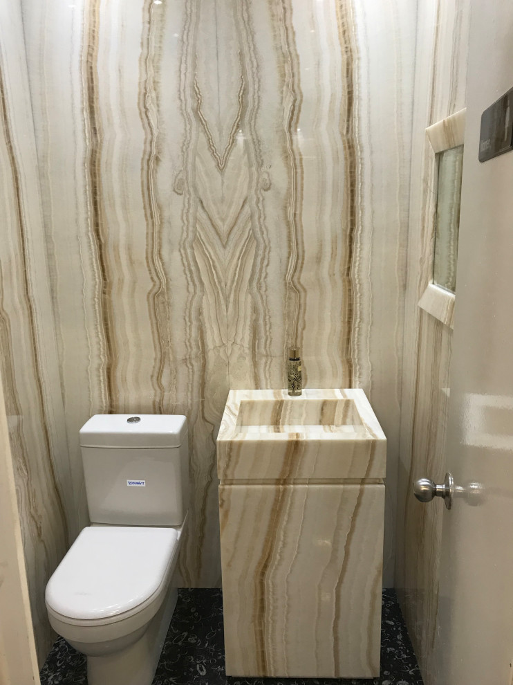 Inspiration for a small modern cloakroom in New York with flat-panel cabinets, beige cabinets, a one-piece toilet, beige tiles, marble tiles, beige walls, slate flooring, an integrated sink, marble worktops, black floors, beige worktops, a freestanding vanity unit, a drop ceiling and panelled walls.