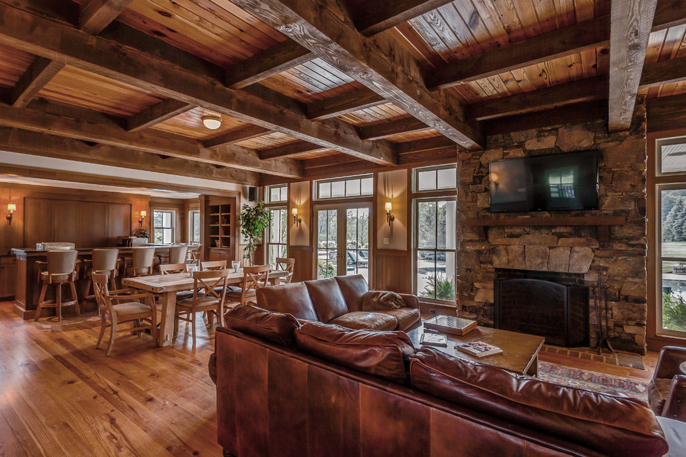Mid-sized country open concept family room in Other with beige walls, medium hardwood floors, a standard fireplace, a stone fireplace surround, a wall-mounted tv and brown floor.