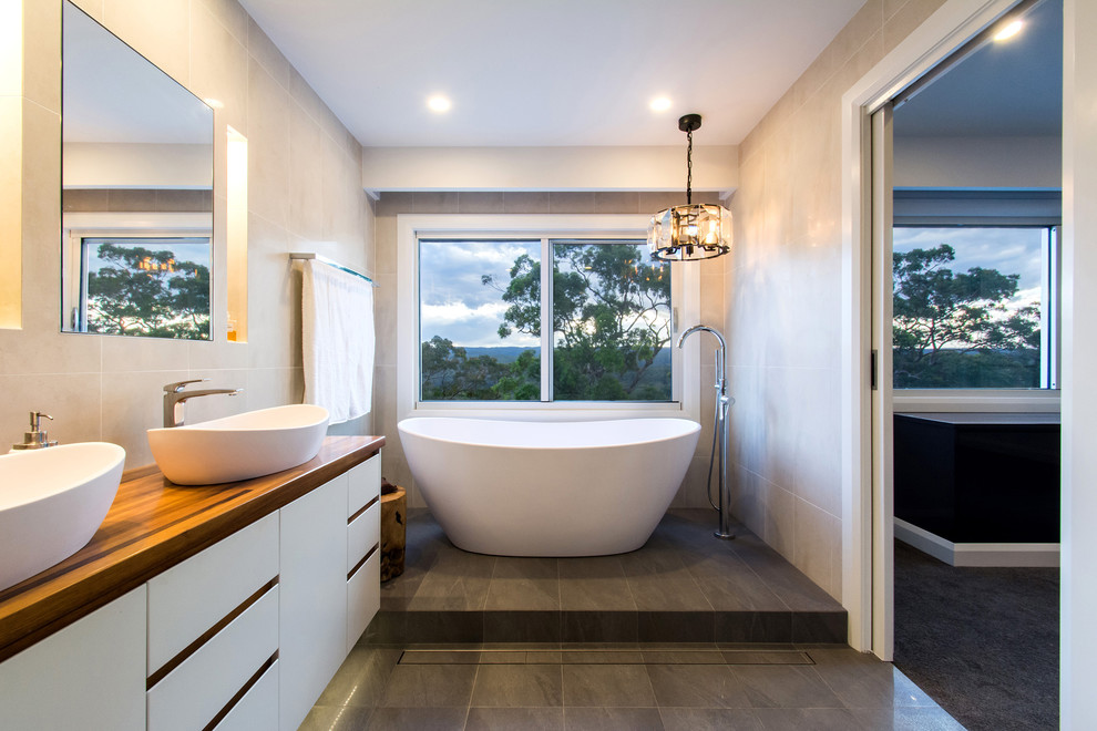 Photo of a mid-sized transitional master bathroom in Sydney with white cabinets, a freestanding tub, beige tile, wood benchtops and grey floor.