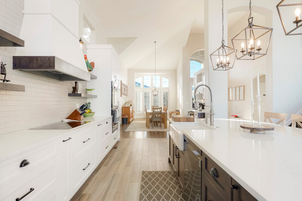 Example of a large transitional single-wall vaulted ceiling open concept kitchen design in Denver with a farmhouse sink, shaker cabinets, white cabinets, white backsplash, subway tile backsplash, black appliances, an island and white countertops