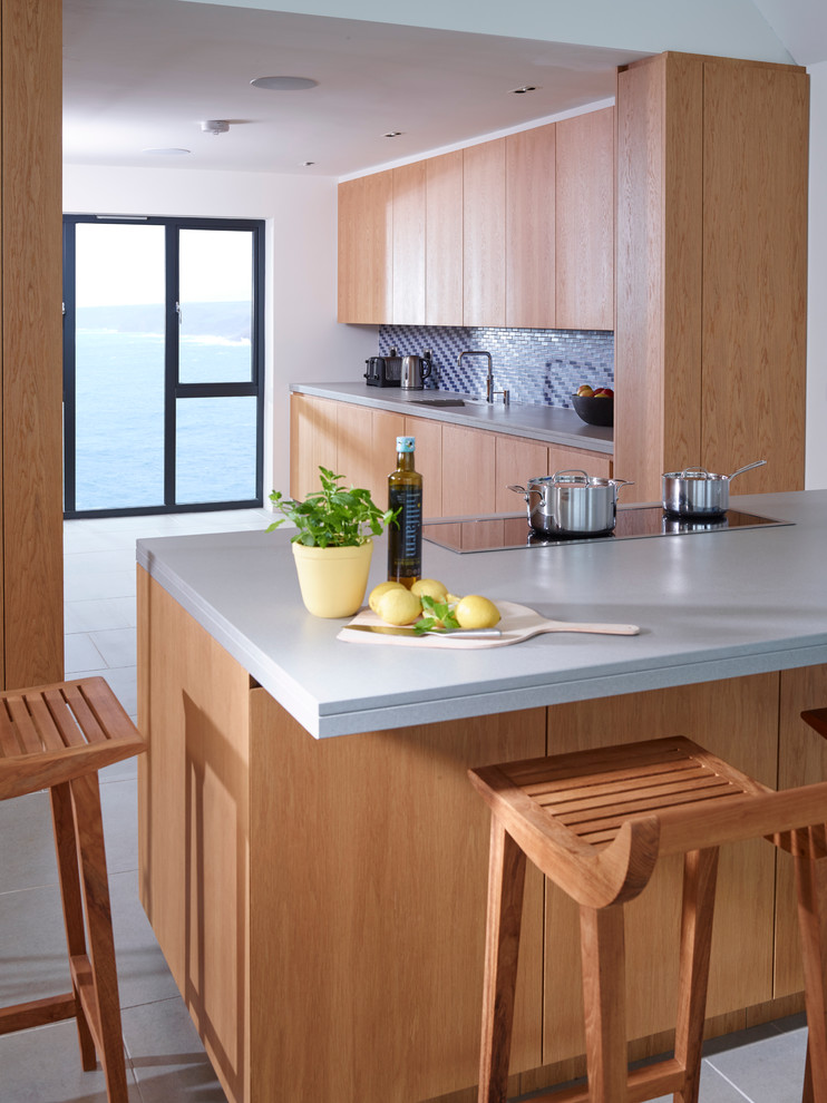 This is an example of a contemporary galley eat-in kitchen in Devon with flat-panel cabinets, light wood cabinets, quartz benchtops, blue splashback, glass tile splashback, stainless steel appliances, ceramic floors and with island.
