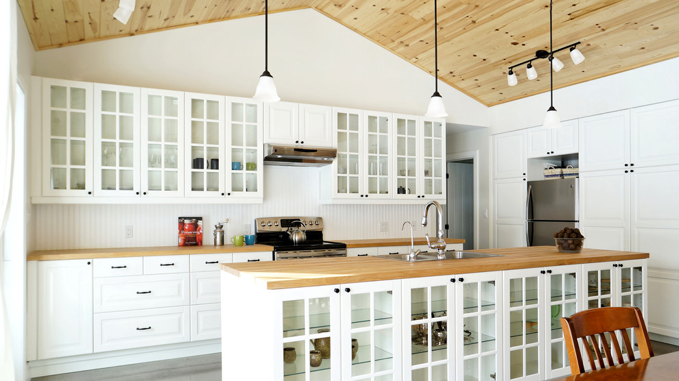 Photo of a country galley open plan kitchen in Toronto with a double-bowl sink, glass-front cabinets, white cabinets, wood benchtops, white splashback and stainless steel appliances.