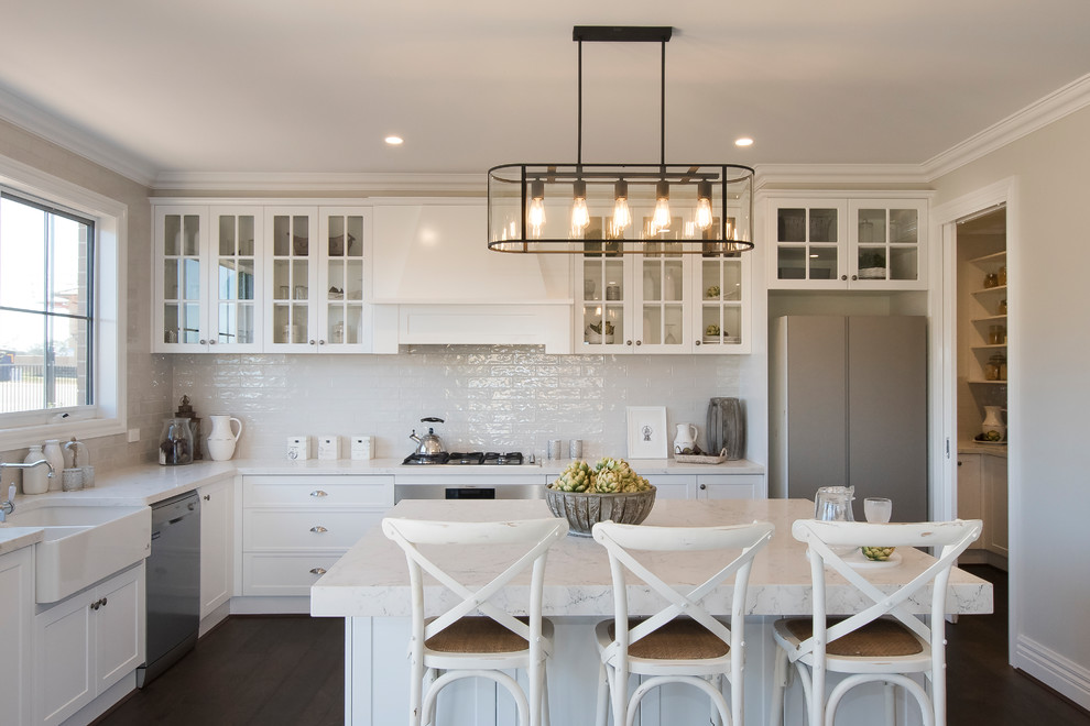 Design ideas for a transitional l-shaped eat-in kitchen in Other with a farmhouse sink, shaker cabinets, white cabinets, white splashback, stainless steel appliances, dark hardwood floors, with island, brown floor and white benchtop.
