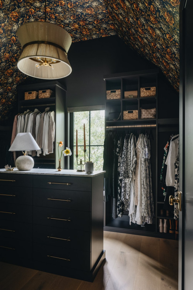 Transitional women's medium tone wood floor, brown floor, vaulted ceiling and wallpaper ceiling walk-in closet photo in Chicago with open cabinets and black cabinets