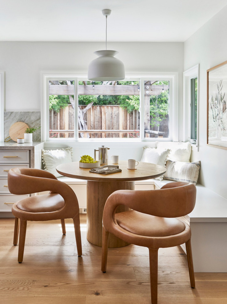 Small traditional dining room in San Francisco with banquette seating, white walls, light hardwood flooring and brown floors.