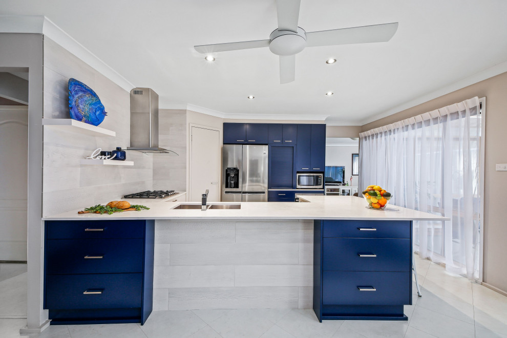 Design ideas for a mid-sized beach style u-shaped eat-in kitchen in Central Coast with an undermount sink, flat-panel cabinets, blue cabinets, solid surface benchtops, subway tile splashback, stainless steel appliances, cement tiles, a peninsula, white floor and white benchtop.