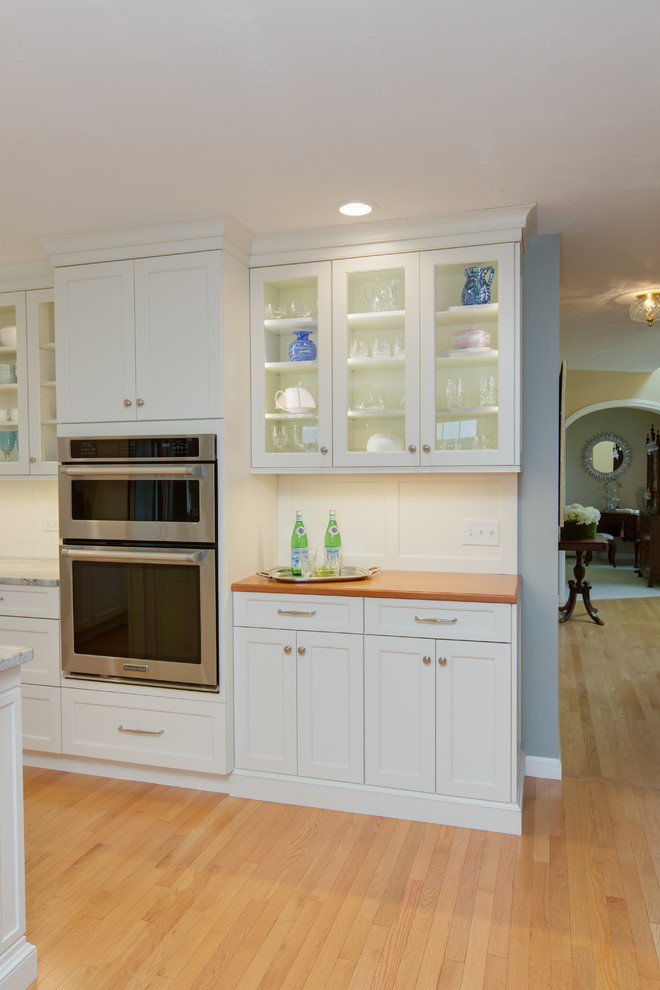 Example of a transitional l-shaped light wood floor eat-in kitchen design in Boston with an undermount sink, recessed-panel cabinets, white cabinets, quartzite countertops, white backsplash, subway tile backsplash, stainless steel appliances and an island