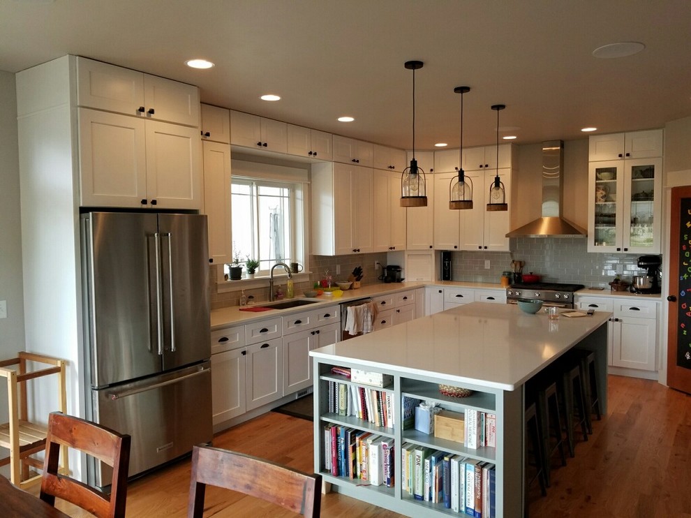 Example of a mid-sized transitional l-shaped medium tone wood floor eat-in kitchen design with an undermount sink, shaker cabinets, white cabinets, quartzite countertops, gray backsplash, ceramic backsplash, stainless steel appliances and an island