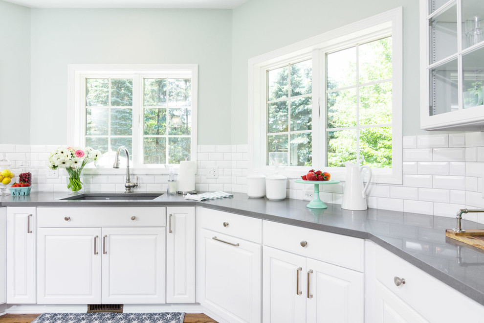 Example of a large transitional u-shaped medium tone wood floor and brown floor eat-in kitchen design in Detroit with an undermount sink, raised-panel cabinets, white cabinets, quartz countertops, white backsplash, ceramic backsplash, an island and white appliances